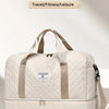 A beige quilted large capacity travel bag with tan straps resting on a white surface.