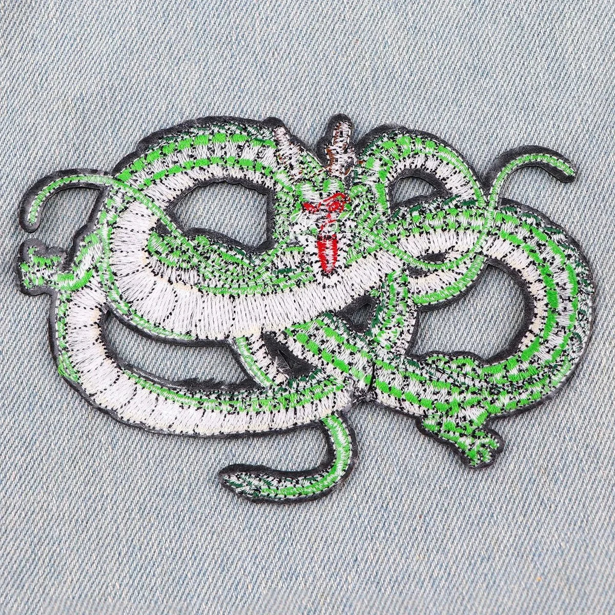 Embroidered patch of a green and white dragon coiled around a red sword on a denim fabric background.