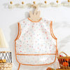 A white baby feeding bib with a sleeveless design and colorful polka dots hanging on a wall.