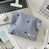 A blue and white plaid makeup bag with floral embroidery resting on a white desk next to a laptop.