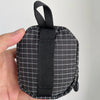 A hand holds a compact EDC utility pouch made of black and white plaid fabric with a black strap.