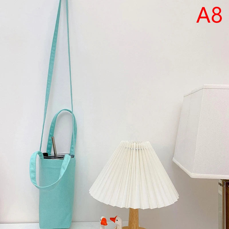 A light blue canvas crossbody bag hanging on a wall next to a white lamp.