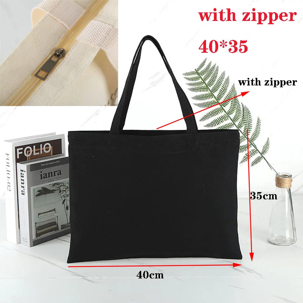 Black canvas tote bag with zipper and bamboo handle, shown next to a glass bottle.