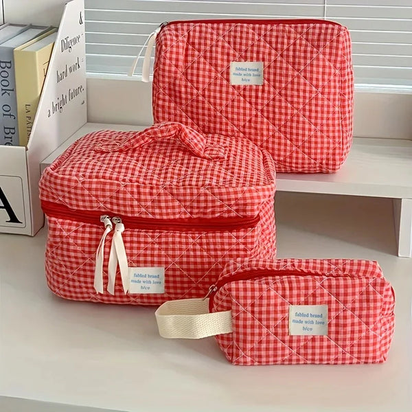 Sac de maquillage à carreaux rouge et blanc avec fermeture éclair, exposé sur une étagère blanche.