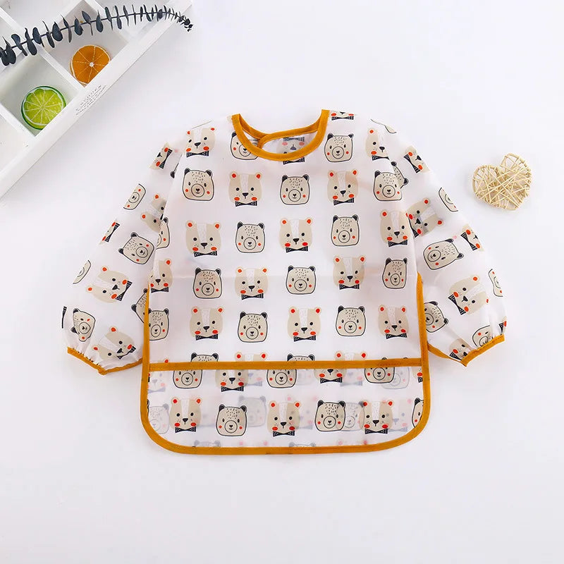 A white long-sleeve baby feeding smock with a repeating pattern of cute animal faces.