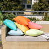 A collection of brightly colored linen-textured outdoor pillow covers in orange, teal, yellow, and pink resting on a light-co