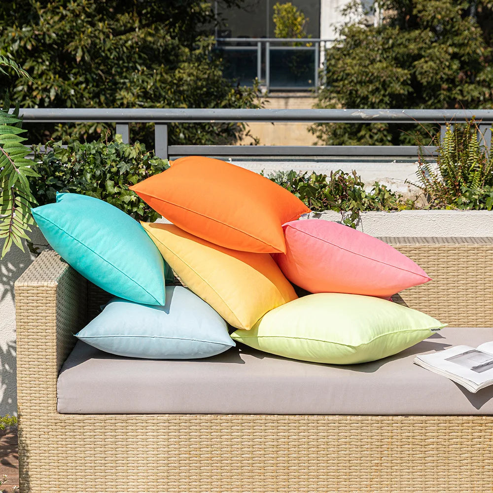 A collection of brightly colored linen-textured outdoor pillow covers in orange, teal, yellow, and pink resting on a light-co