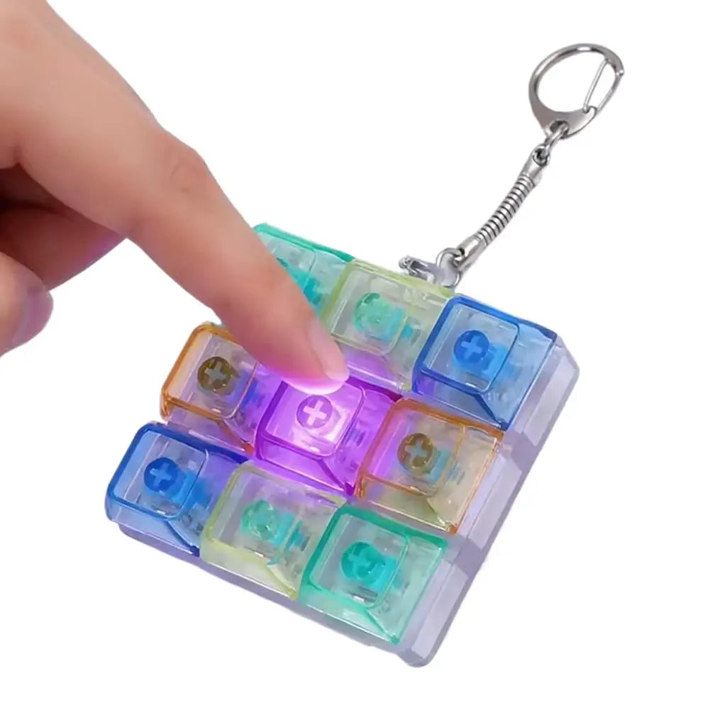 Una mano sostiene un llavero de teclado mecánico mini con múltiples luces LED de colores en un aro plateado.
