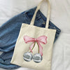 A canvas tote bag with a pink bow and two silver spherical charms resting on a white sheet.