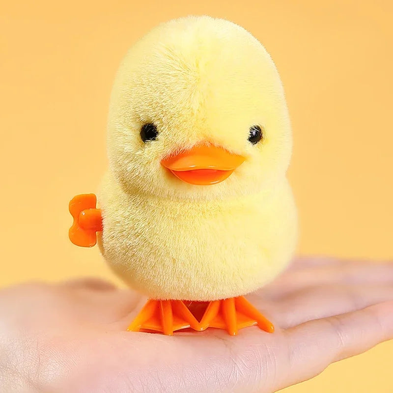 A yellow wind-up walking chicken toy with orange feet is held in a person's hand.