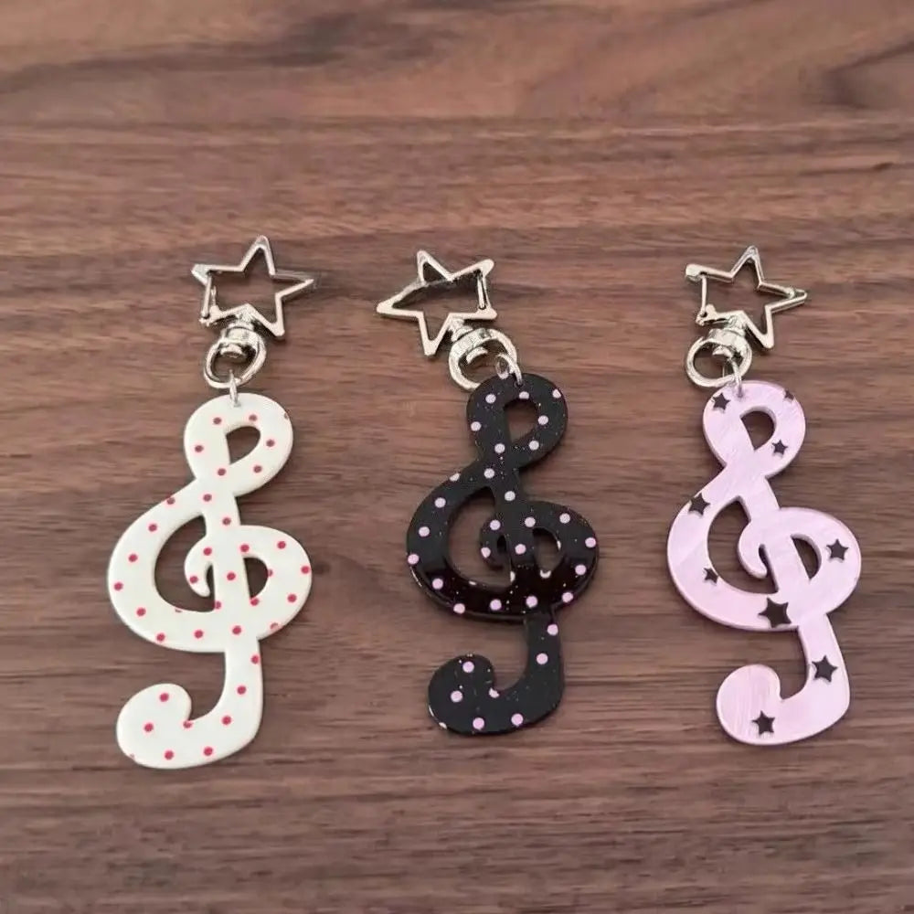 Trois porte-clés de notes de musique en acrylique blanc, noir et rose avec des charms étoiles argentées