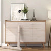 A light wood grain wallpaper roll is displayed on a wooden cabinet with framed art and a small plant.