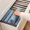 A hand is placing folded blue fabric items into a light gray drawer organizer for clothing.