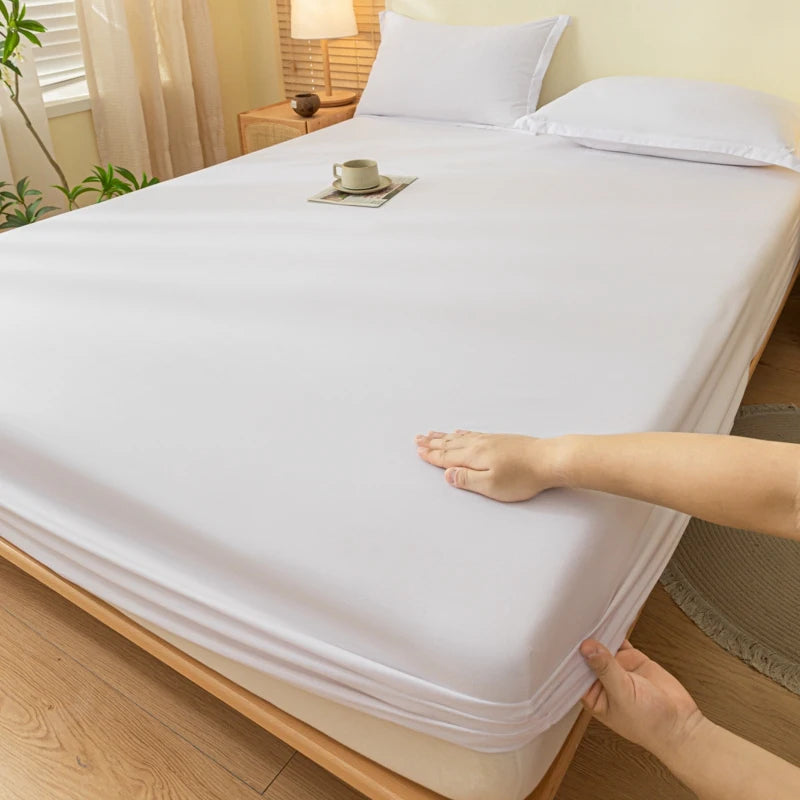 A hand is touching a white fitted sheet on a bed, showing the fabric texture and elastic edge.
