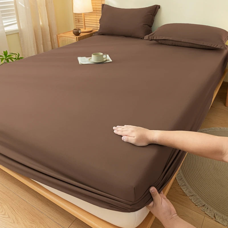 A brown fitted sheet is draped over a bed, with a hand adjusting the fabric.