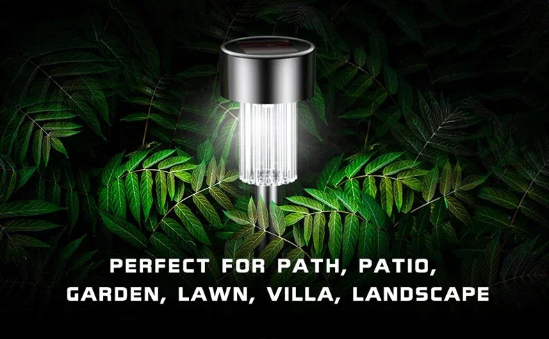 A silver solar powered garden lantern light with a clear glass shade surrounded by green foliage.