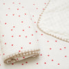 White cotton gauze baby swaddle blanket with a delicate bear print and pink hearts scattered on a white background.
