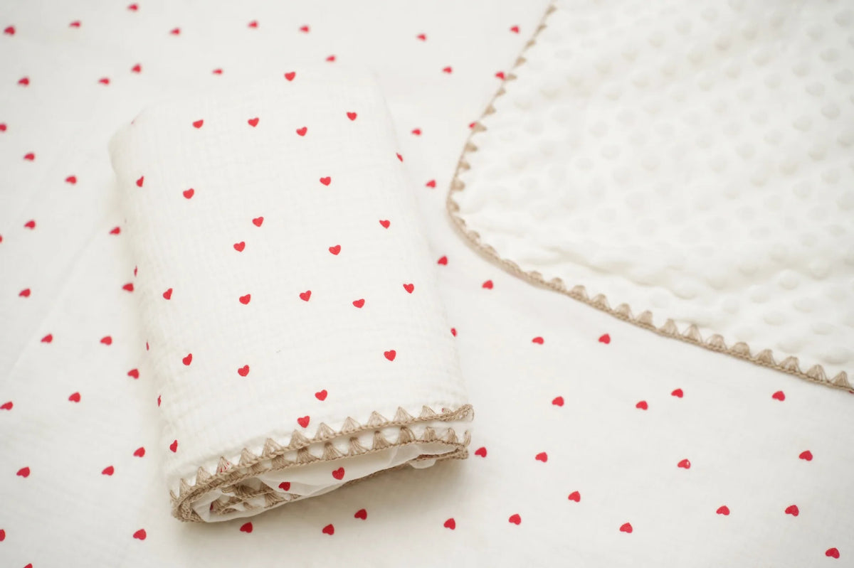 White cotton gauze baby swaddle blanket with a delicate bear print and pink hearts scattered on a white background.