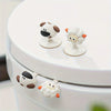 A white toilet seat with decorative cartoon animal lifter handles in brown and white.