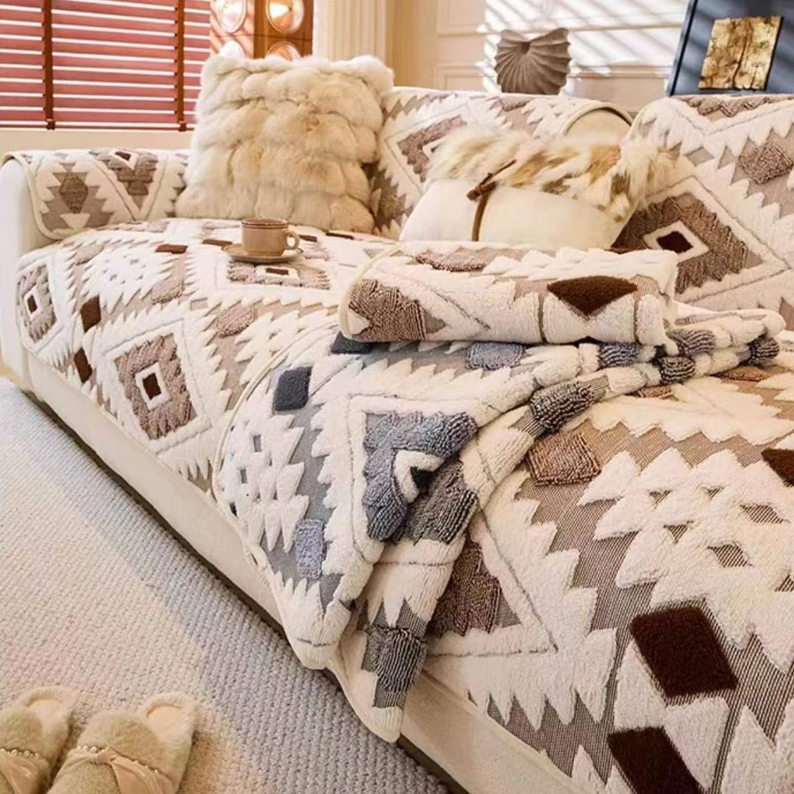 Una funda de sofá de forro polar beige y marrón con cojines de piel sintética sobre una cama de color claro.