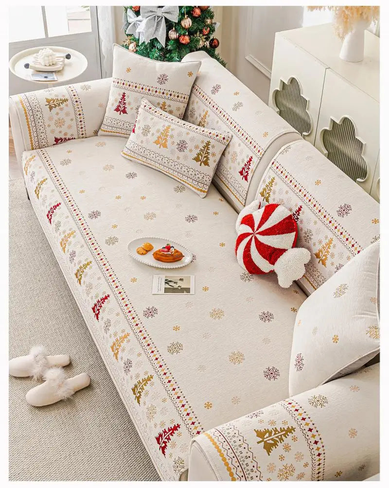 A beige sofa covered with Christmas tree patterned fabric and decorative pillows on a light rug.