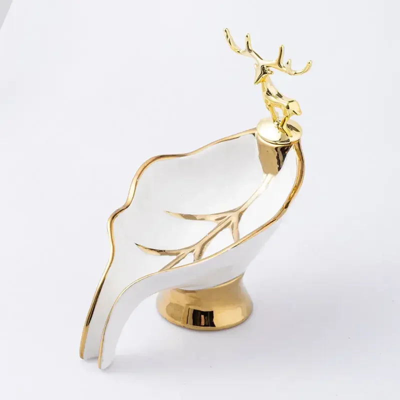 A white ceramic soap dish shaped like a leaf with a gold-colored drain rack and deer antlers.