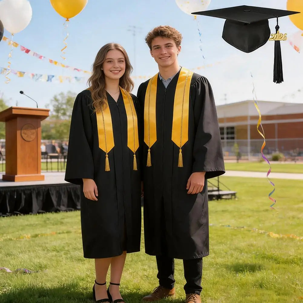 Two young adults in black graduation gowns and caps stand outdoors on a grassy field.