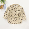 A beige waterproof long-sleeve smock for toddlers with a black polka dot pattern.
