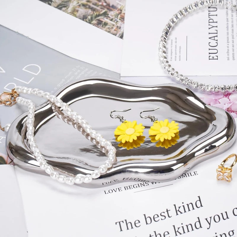 A silver cloud-shaped tray holds pearl necklaces and yellow floral earrings.