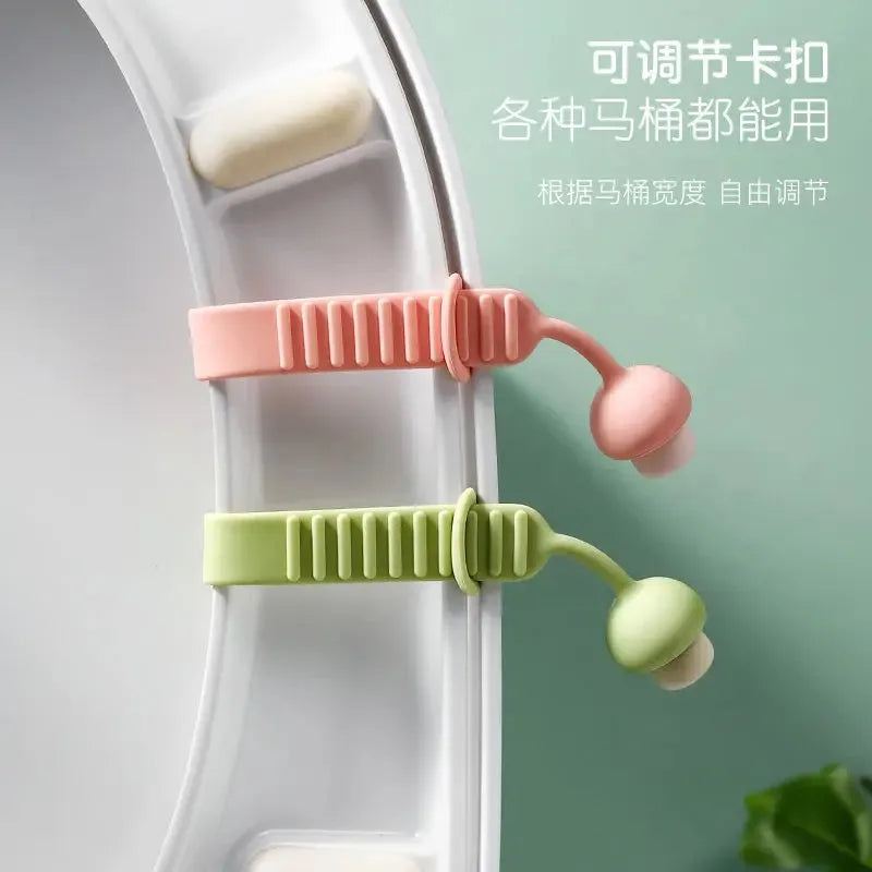 A silicone toilet seat lifter in pink and light green colors is shown being used to lift a toilet seat.