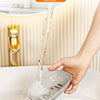 A hand is pouring water into a white double-layered draining soap dish in a bathroom sink.
