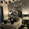 A birthday decoration featuring a silver and black balloon garland with oversized foil numbers on a bed.