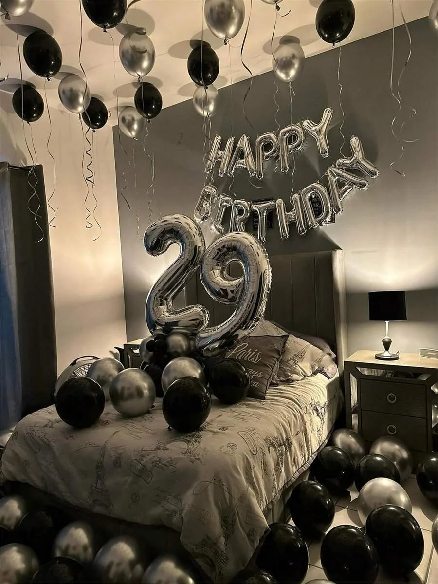 A birthday decoration featuring a silver and black balloon garland with oversized foil numbers on a bed.