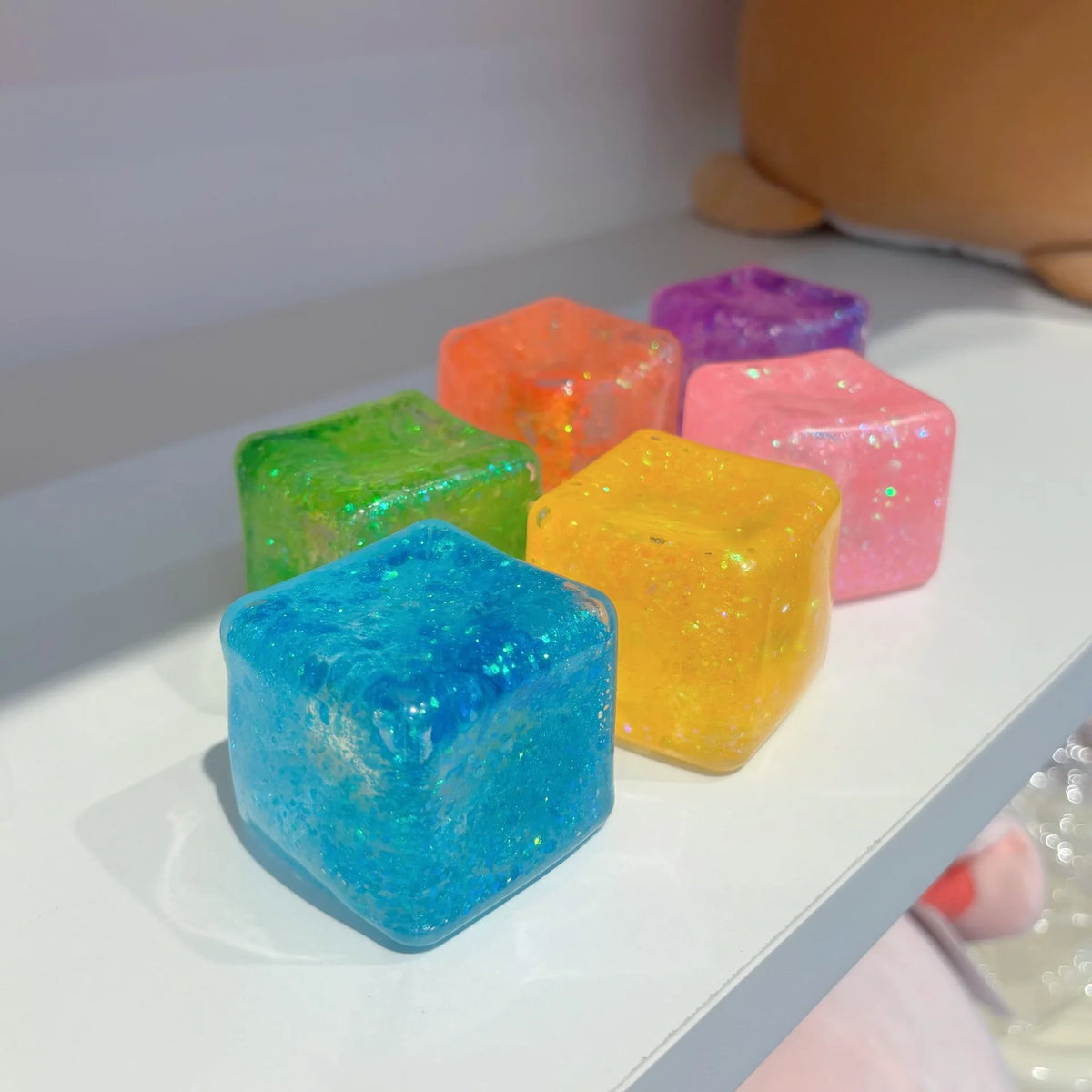 Eine Sammlung farbenfroher quadratischer Stressball-Fidget-Spielzeuge in Grüntönen, Orange, Violett und Gelb ausgestellt