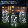 Three vertical solar firecracker willow lights illuminating a lawn in front of a house.