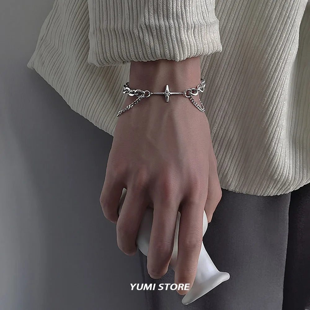 Gros plan d'une main portant un bracelet argenté à double étoile et croix sur un poignet, sur fond neutre.
