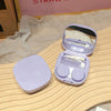 A light purple compact contact lens travel case with a hinged lid is displayed on a wooden surface.