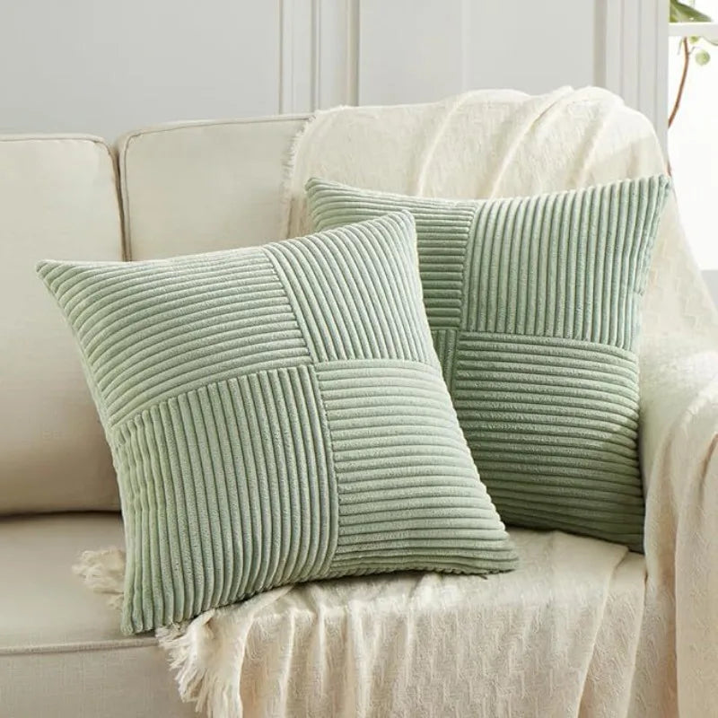 Two light green corduroy patchwork throw pillow covers with vertical stitching on a white sofa.
