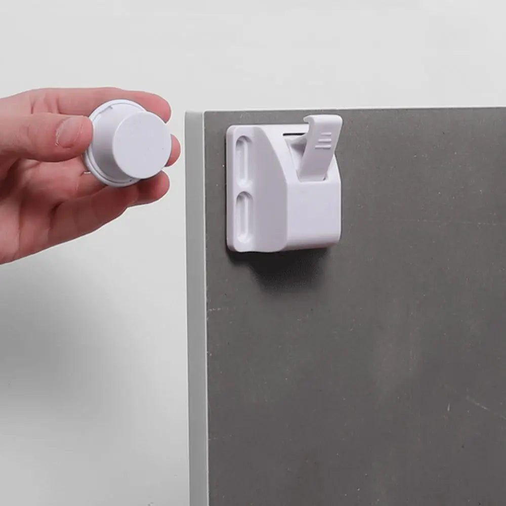 A hand is holding a white magnetic cabinet lock and placing it onto a gray cabinet door.