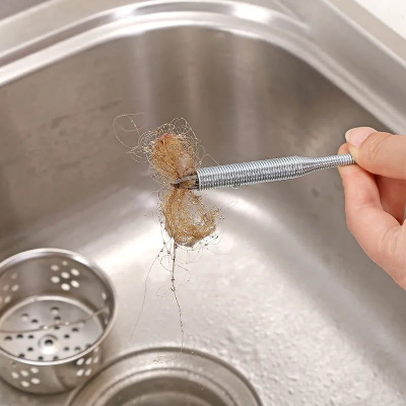 Une main utilise un serpent de nettoyage pour évier pour retirer des cheveux d'un siphon de cuisine.