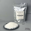 A white bag of Natural Soybean Wax flakes next to a pile of the same wax on a dark plate.