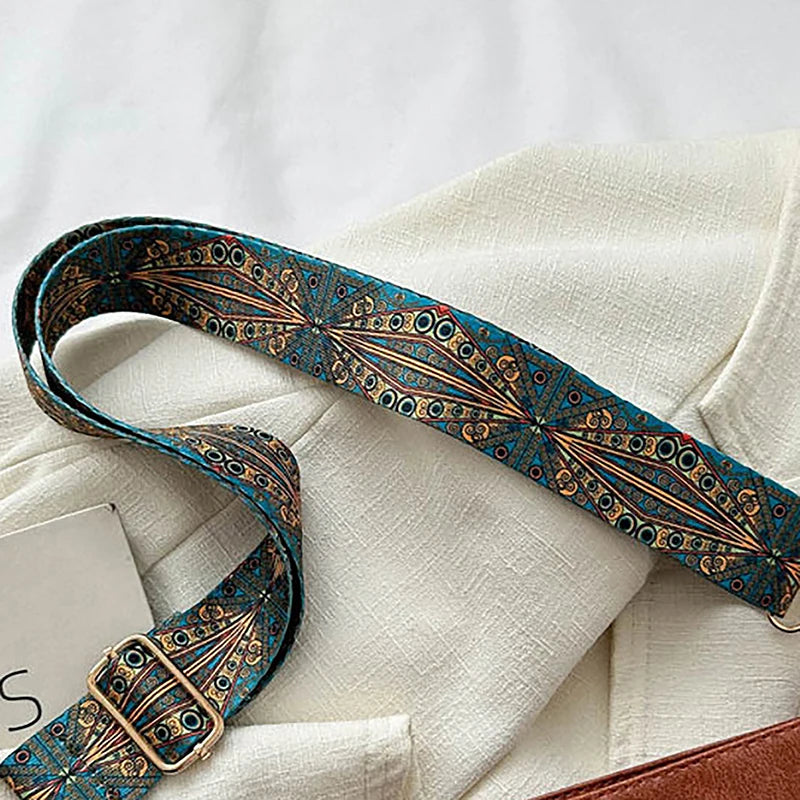 Sac à main à bandoulière géométrique large, motif bleu sarcelle et or, posé sur un tissu en lin crème.