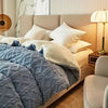 A bed with a light beige duvet and blue textured blanket in a modern bedroom setting.