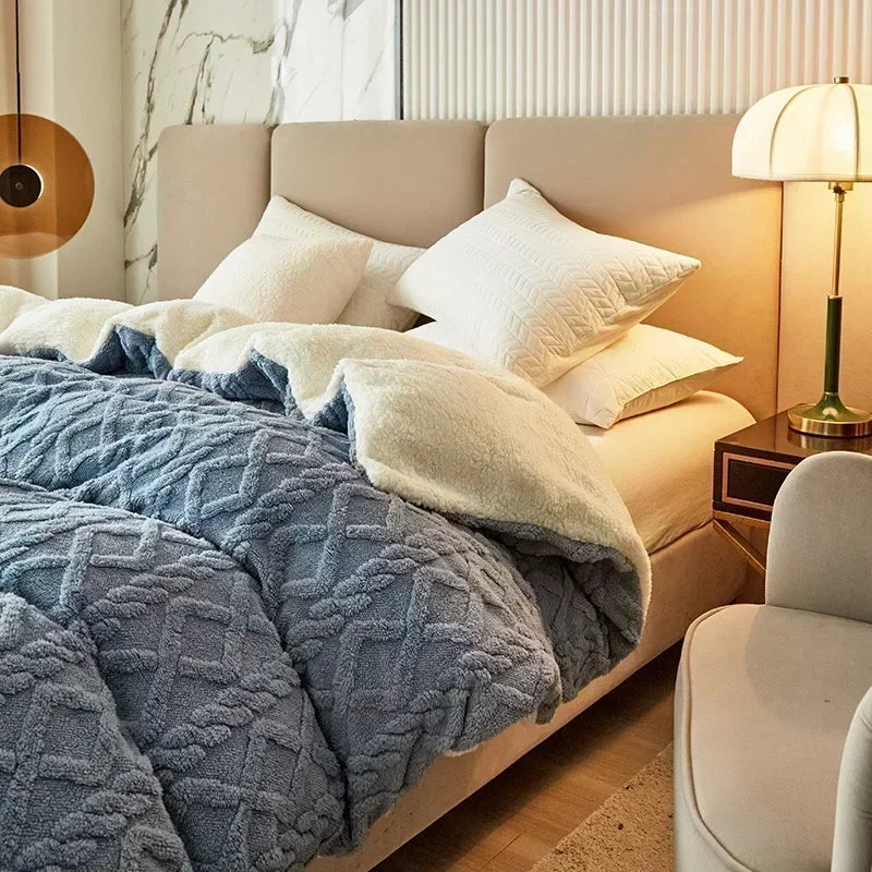 A bed with a light beige duvet and blue textured blanket in a modern bedroom setting.
