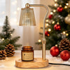 A brass electric candle warmer lamp with a textured glass shade sits on a wooden surface near a decorated Christmas tree.