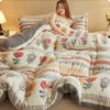 A cozy, patterned plush throw blanket featuring floral and geometric designs is draped over a bed.