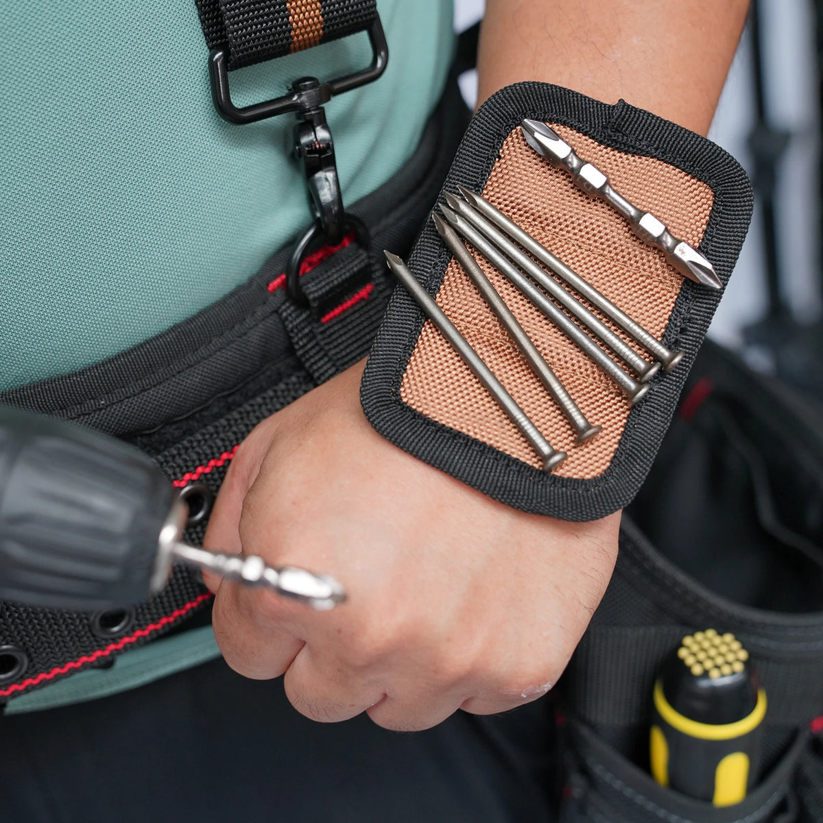 A hand is using a magnetic tool to attach or detach a black wrist strap with a phone holder and suspenders.