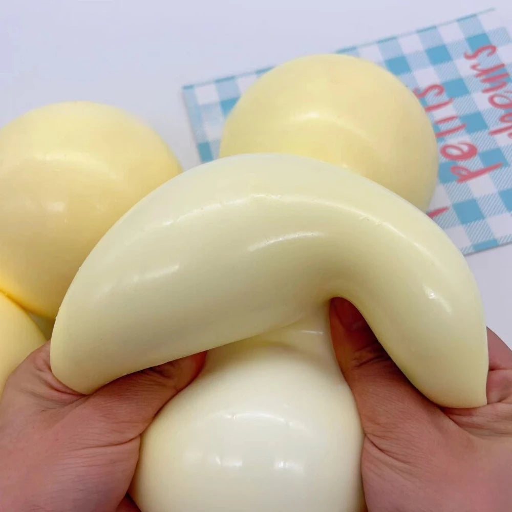 Eine Hand hält einen großen, blassgelben sensorischen Stressabbau-Squishy-Ball vor einem blau-weißen Muster.