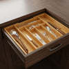 A wooden drawer organizer with bamboo inserts holding various silverware and utensils.