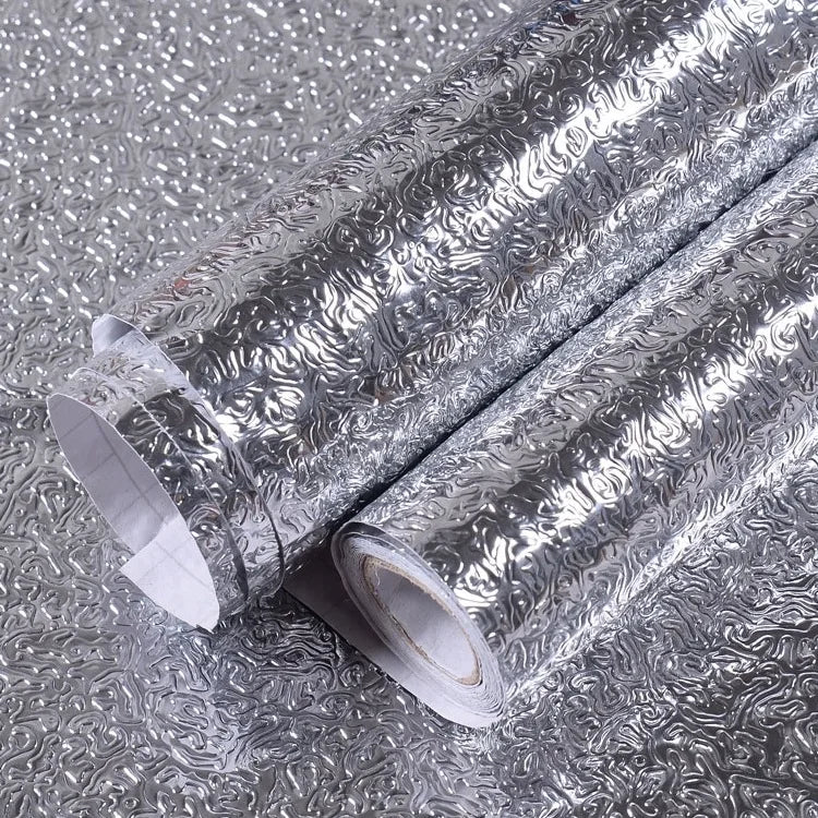 Rolls of silver aluminum foil peel-and-stick kitchen backsplash wall stickers lying on a gray surface.